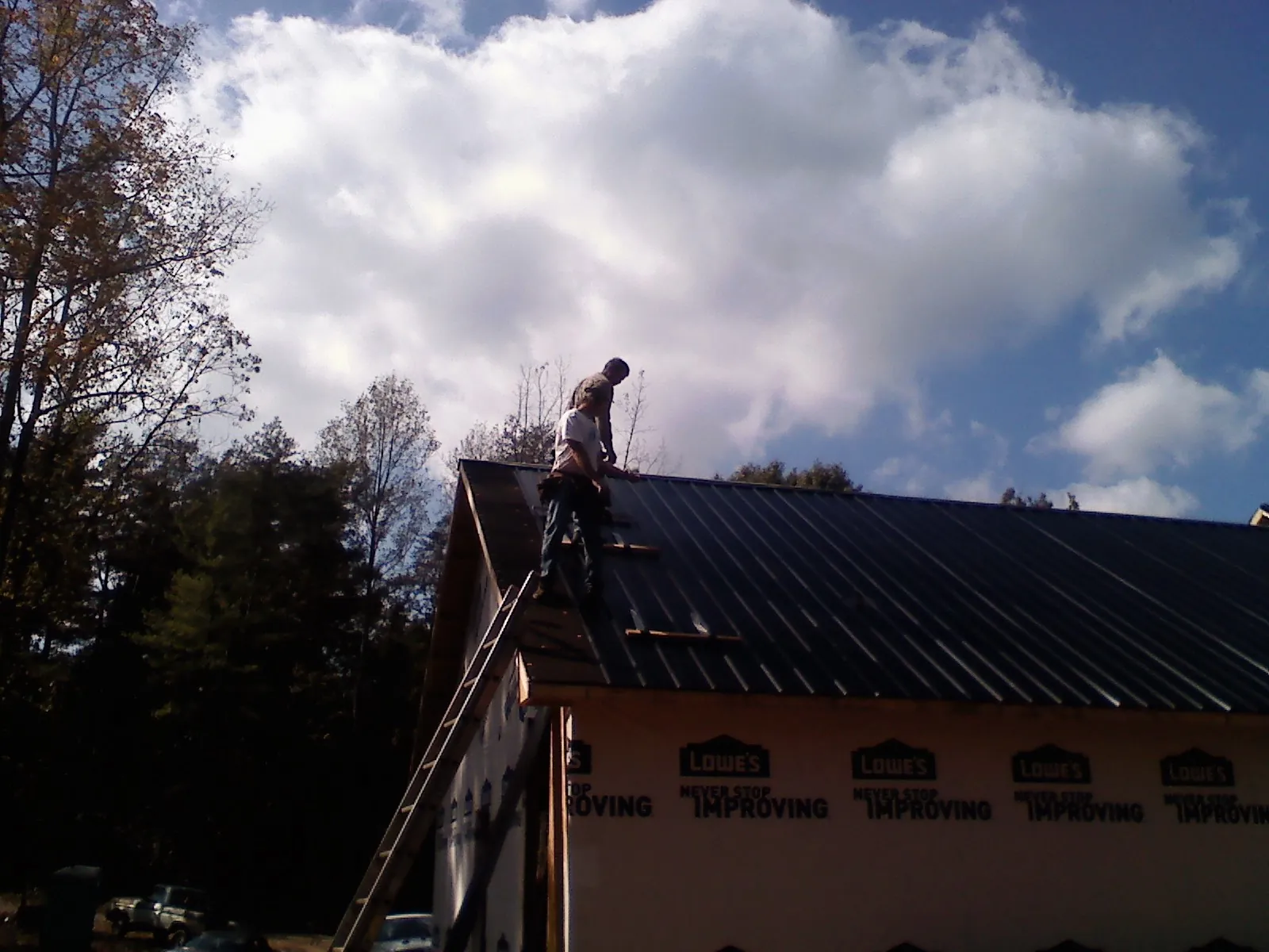 Roofer fastening dark metal panels high against a cloudy sky, from a Roof Inspection job in Worth