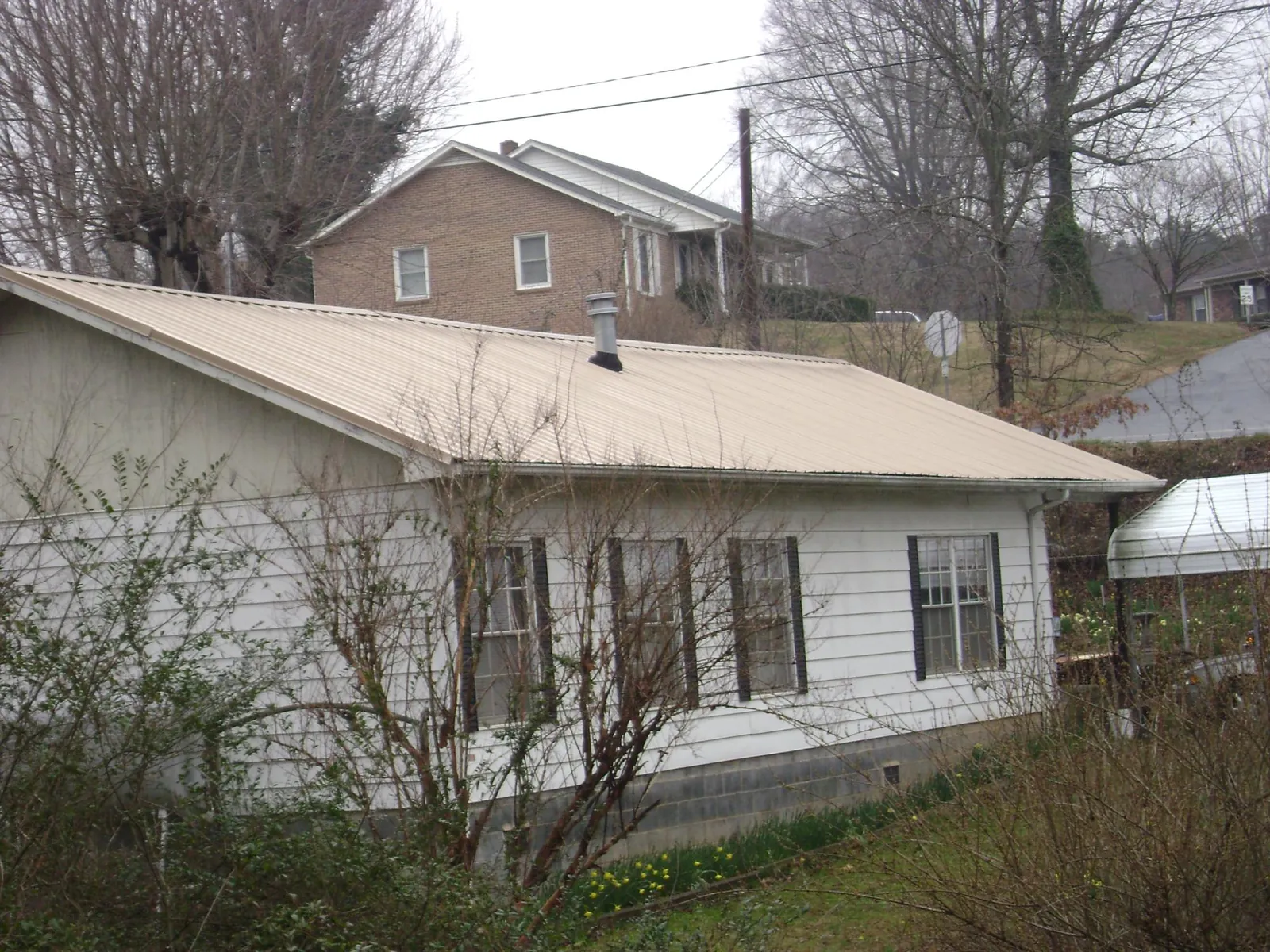Tan metal roof on a white sided house set into a hillside — Commercial Roofing by Roofing Brothers in Worth